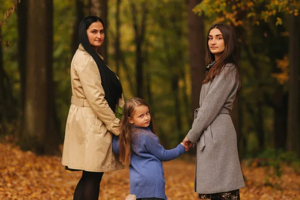 Mom and two daughter have fun in ther park. Youngest daughter collect leaves and smile. Happy family walking in the forest