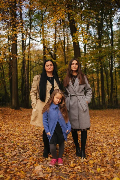 Mom and two daughter have fun in ther park. Youngest daughter collect leaves and smile. Happy family walking in the forest