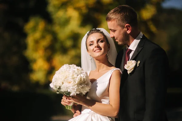 Bella sposa con suo marito nel parco. Stanno camminando vicino all'albero giallo. Bellissimo trucco — Foto Stock