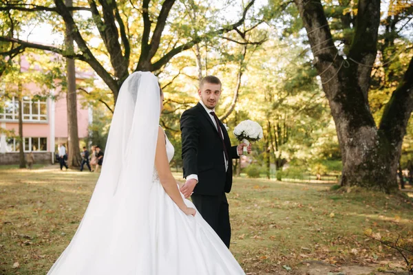 Giovane sposa con sposo che cammina nella foresta. Donna con abito lungo bianco e uomo in abito nero con cravatta — Foto Stock