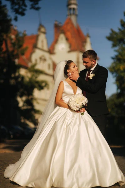O noivo e a noiva estão em frente ao castelo. Mulher segurar buquê de flor branca nas mãos — Fotografia de Stock