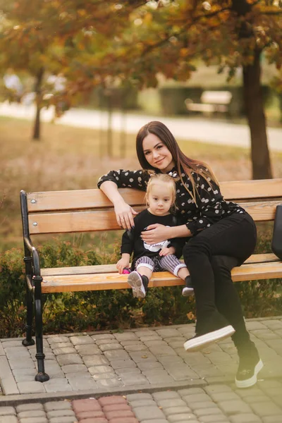 Boldog anya és lánya játszik őszi parkban. Család, életmód koncepció. Őszi idő. Anya és lánya ül a padon — Stock Fotó