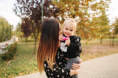 Anne ve küçük kızı sonbahar havasında yürüyorlar. Şık küçük kızı ve onun güzel annesi. Mutlu çocukluk. Mutlu bir ailenin açık hava portresi. İyi eğlenceler