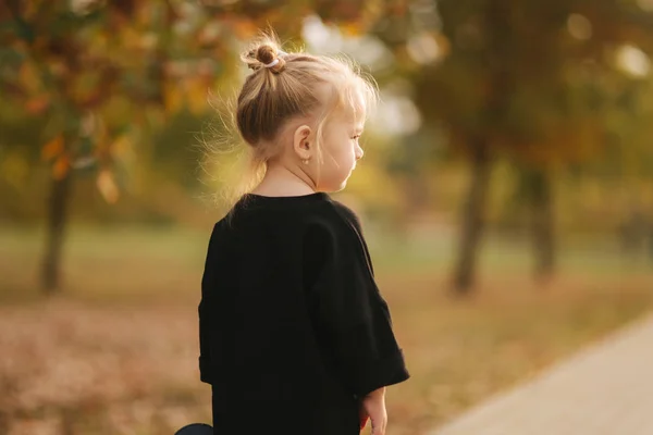 Портрет маленькой девочки, идущей в роли осенью. Блондинка на улице. Теплая осень. Вид сзади на прогулку ребенка — стоковое фото