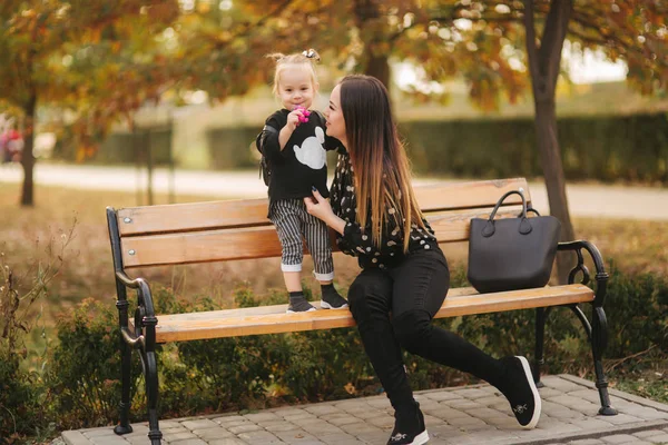 Gelukkige moeder en haar dochter spelen in Autumn Park. Familie, lifestyle concept. Herfst tijd. Moeder en dochter zittend op de Bank — Stockfoto