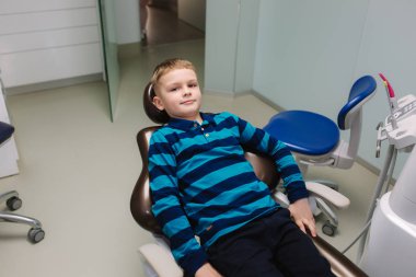 Ofisteki dişçi koltuğunda oturan genç bir çocuk. Çocuk diş hekimi muayenesi bebek dişleri