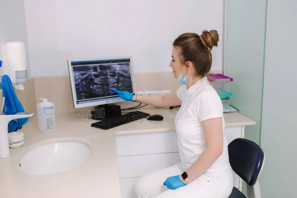 Young female dentist sitting by the monitor with x-ray