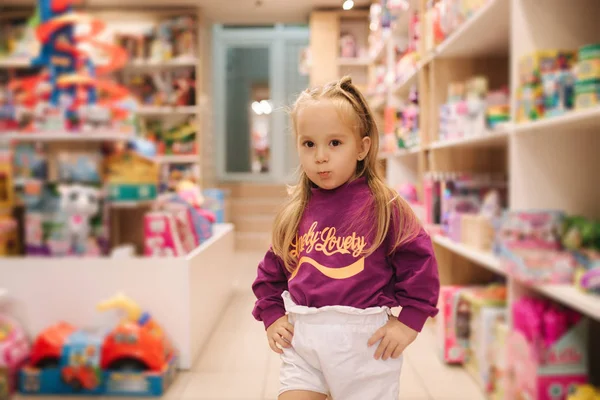 Adorable little girl shopping for toys. Cute female in toy store. Happy young girl selecting toy — Stockfoto