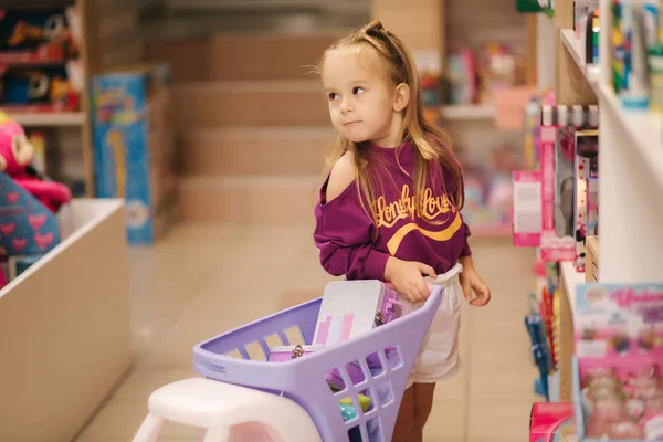 Kislány kis bevásárlókosár gyerekek plázában. Boldog lány választotta, hogy mit vásárolnak a játékboltban — Stock Fotó
