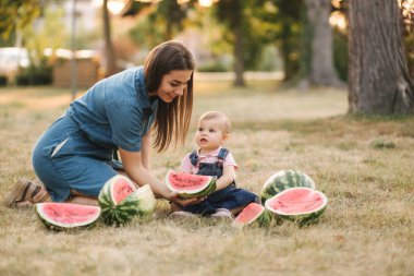 Anne ve kızı yazlık parkta karpuz yiyor. Küçük kız çimenlerin üzerinde oturur. Mutlu aile birlikte vakit geçirmek