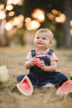 Sevimli kız bebek yakın karpuz yemek. Denim elbiseli şık bebek. Güzel çocuk açık havada meyve yemek