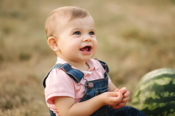 Primer plano de adorable niña comer sandía. Elegante bebé en vestido de mezclilla. Hermoso niño comer fruta al aire libre — Foto de Stock