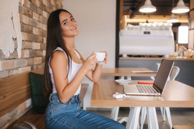 Kahve içen ve kafede dizüstü bilgisayarda çalışan genç bir kadın. Akıllı kadın internette para kazanıyor. Kafede öğrenci eğitimi.
