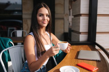 Young business lady work on laptop and drinking a coffee. Beautiful girl sitting in cafe outside. Woman using phone