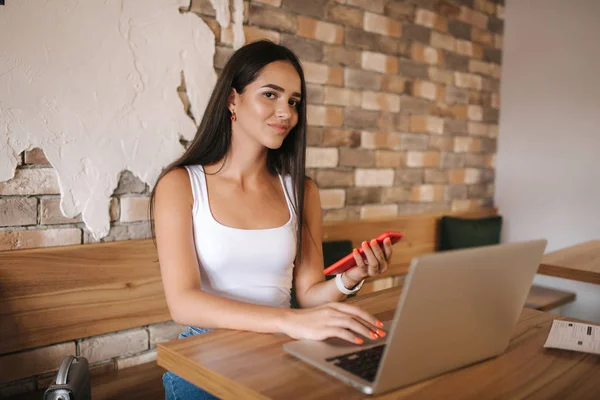 Привлекательная девушка работает на ноутбуке в кафе. Красивая девушка использует компьютер для работы. Девушка пьет капучино в кафе. Ольнильская работа, фрилансер — стоковое фото