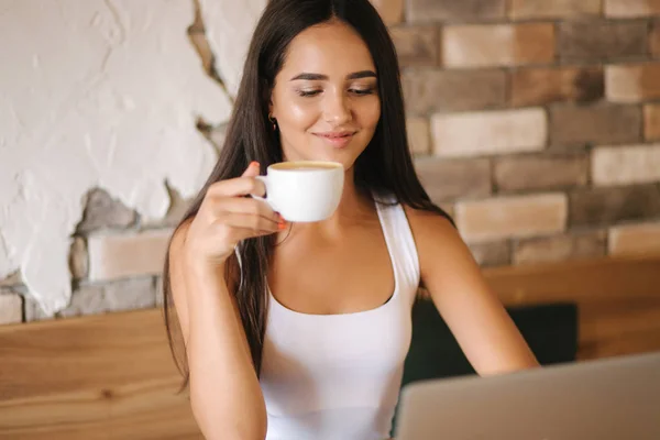 Közelkép egy lányról, aki cappuccinót iszik a kávézóban. Gyönyörű barna. — Stock Fotó