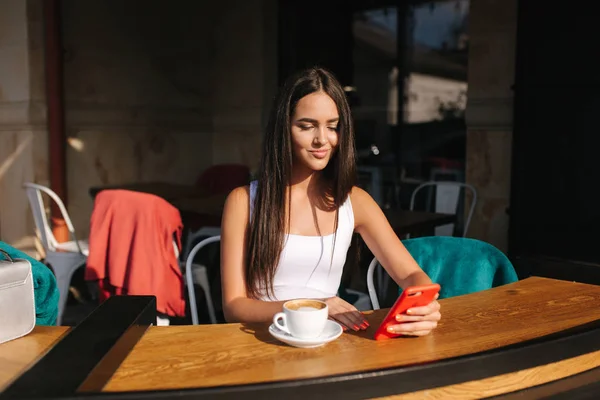Aantrekkelijke jonge vrouw met behulp van telefoon in het café. Mooie brunette meisje chatten — Stockfoto