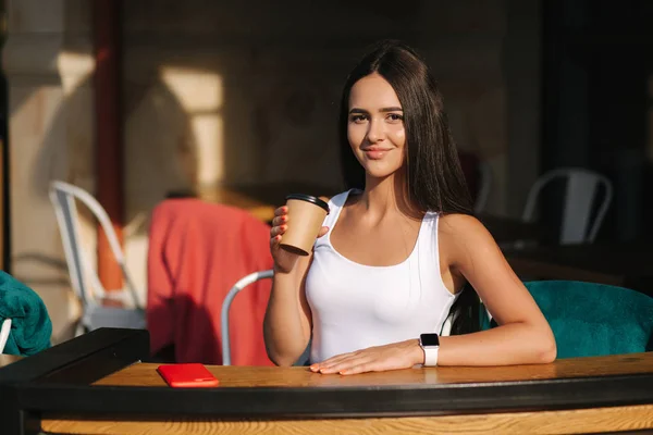 迷人的女孩在咖啡馆的露台上用工艺杯喝杯咖啡。美丽的黑发 — 图库照片