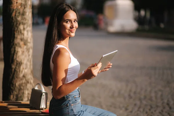 Hermosa chica utilizar la tableta fuera. Mujer sentada en el banco. Día caliente de verano — Foto de Stock