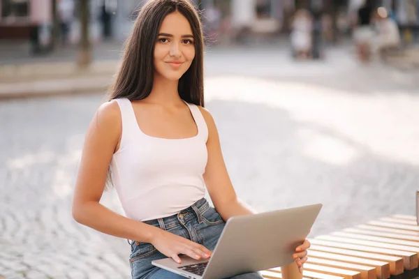 Aantrekkelijke jonge vrouw in gebruik laptop buiten op de banch in de zomertijd. Mooie brunette vrouwelijke student studie — Stockfoto