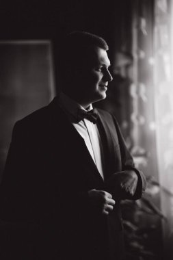 Mutlu damat evdeki pencerenin yanında duruyor. Damat sabahı. Takım elbiseli yakışıklı adam