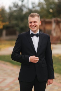 Sonbahar 'da gelinlik giymiş yakışıklı bir damat. Sarı ağacın arka planı. Siyah takım elbiseli, güzel papyonlu adam.