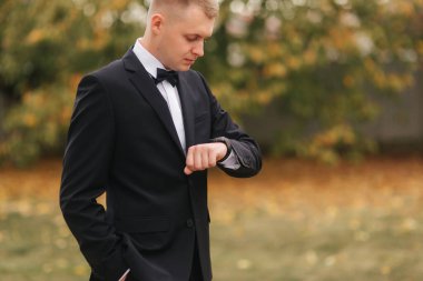 Sonbahar 'da gelinlik giymiş yakışıklı bir damat. Sarı ağacın arka planı. Siyah takım elbiseli, güzel papyonlu adam.