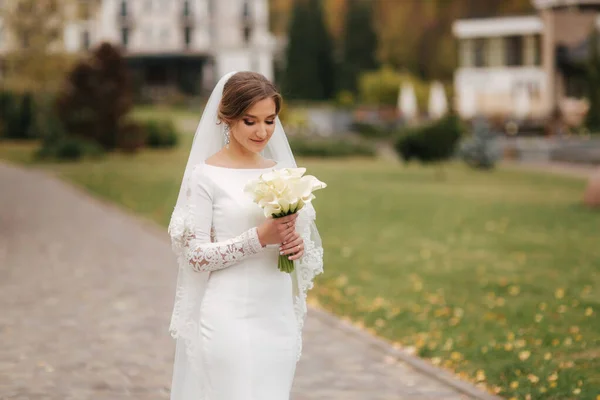 Bela noiva em elegante vestido de noiva ficar no parque e segurar um buquê de flores. Retrato de senhora encantadora — Fotografia de Stock
