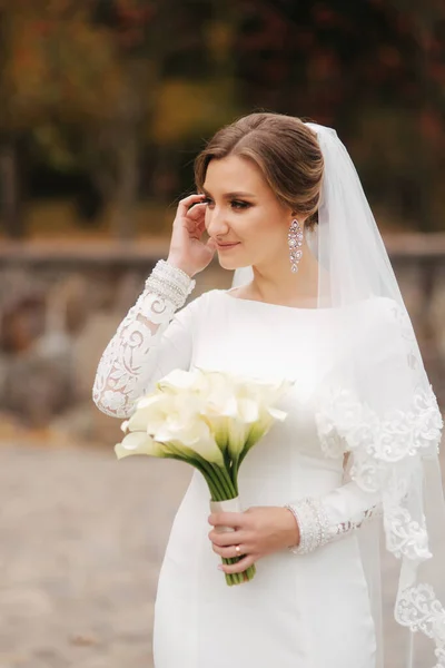Schöne Braut in elegantem Brautkleid stehen im Park und halten einen Strauß Blumen. Porträt der charmanten Dame — Stockfoto