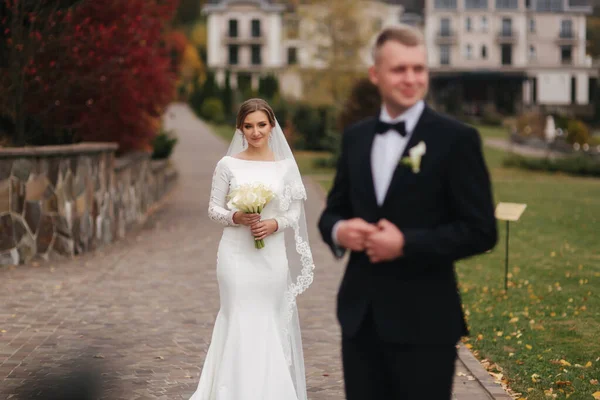 Stylový pár procházející se v parku v jejich svatební den. Šťastní novomanželé venku v podzimním počasí. Ženich skvrny před nevěstou — Stock fotografie