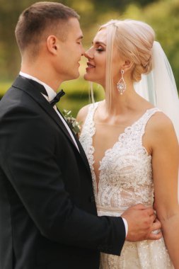 Yakışıklı damat güzel gelini sarıl. Parkta yürüyüş yeni evliler. Zarif gelinlik sarı saçlı kadın