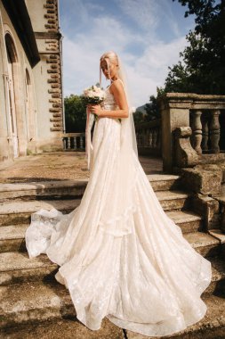 Muhteşem gelin gelinlikle merdivende palace tarafından ayakta. Bir buket çiçek tutun