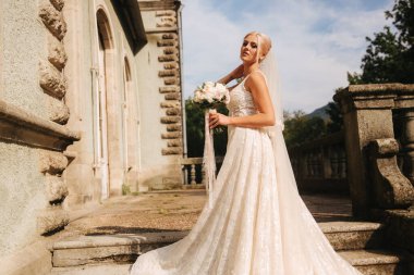 Muhteşem gelin gelinlikle merdivende palace tarafından ayakta. Bir buket çiçek tutun