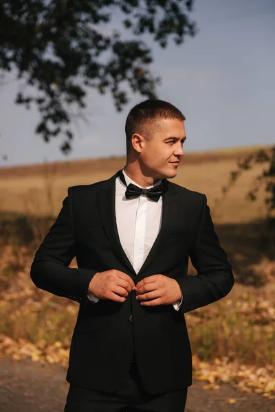 Young man walking in the park. Handsome groom in black suit — Stock Photo, Image