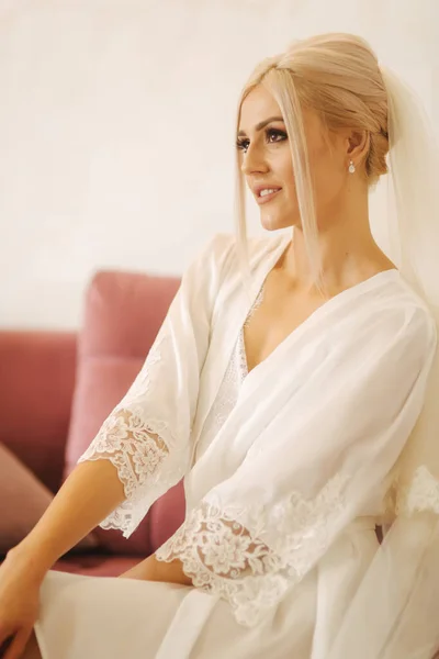 Ráno krásné blond vlasy nevěsta v blízkosti svatební šaty do odcházející bílé negližé — Stock fotografie