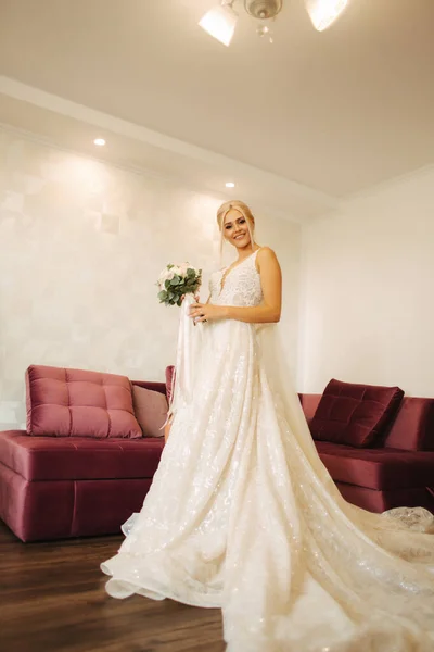 Noiva elegante em belo vestido de noiva com buquê em casa. Mulher de cabelo loiro com bela maquiagem e penteado — Fotografia de Stock