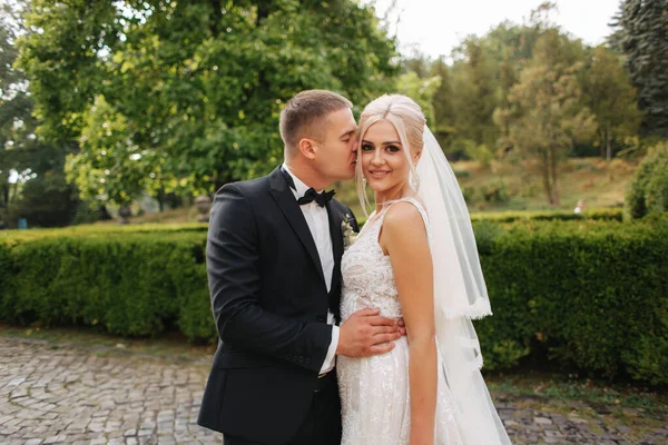 Knappe bruidegom knuffel zijn mooie bruid. De pasgetrouwden wandelen in het park. Blond haar vrouw in elegante trouwjurk — Stockfoto
