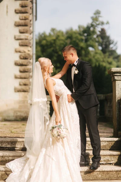 O noivo e a noiva estão nas escadas. Modelo de moda em roupas elegantes. Vestido longo branco e terno elegante — Fotografia de Stock