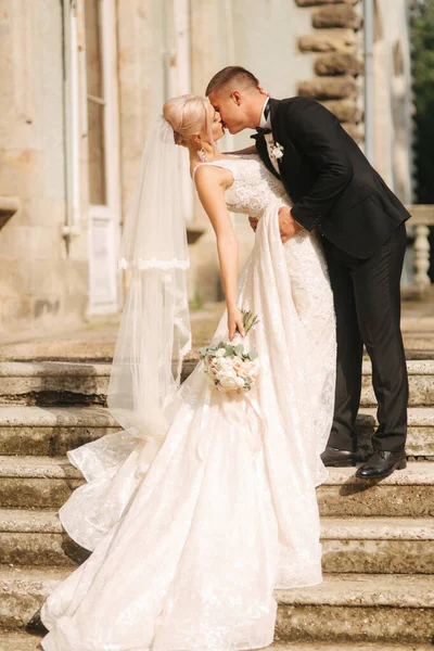 O noivo e a noiva estão nas escadas. Modelo de moda em roupas elegantes. Vestido longo branco e terno elegante — Fotografia de Stock