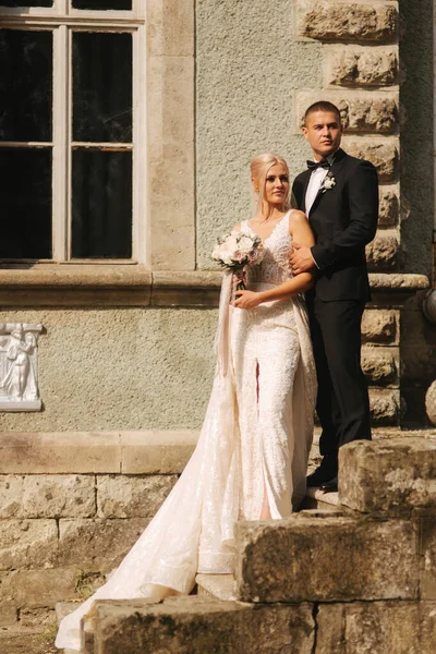 Жених и невеста стоят на лестнице. Мода модели в элегантной одежде. Белое длинное платье и стильный костюм — стоковое фото