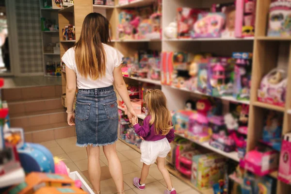 和妈妈一起去买玩具的可爱小女孩的倒影。 可爱的女孩和妈妈在玩具店里。 快乐的家庭选择玩具 — 图库照片