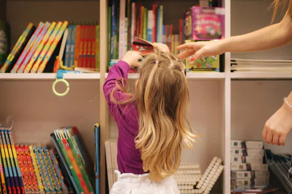 Вид сзади на очаровательную маленькую девочку, покупающую игрушки. Милая женщина в магазине игрушек. Счастливая девушка выбирает игрушку — стоковое фото