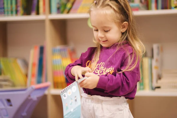 Niña con carrito de compras pequeño en el centro comercial para niños. Chica feliz elegir qué comprar en la tienda de juguetes — Foto de Stock