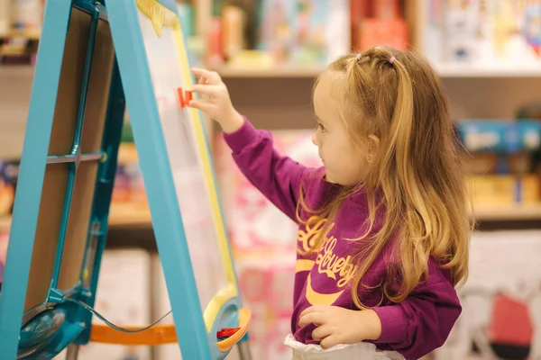 Adorável menina desenha na mesa na loja de crianças — Fotografia de Stock