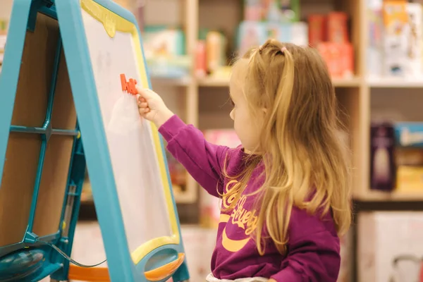 Adorable niña dibuja en el escritorio en la tienda de niños — Foto de Stock