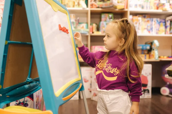 Adorable niña dibuja en el escritorio en la tienda de niños —  Fotos de Stock