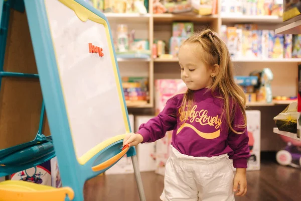 Adorable niña dibuja en el escritorio en la tienda de niños — Foto de Stock