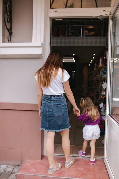 Aranyos kislány az anyjával bemegy a játékboltba. Boldog gyerek játékokat választ anyával. Anya és lánya játékokat vesznek a gyerekboltban. — Stock Fotó