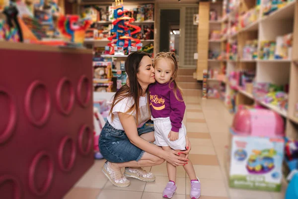 可爱的小女孩和她的妈妈去玩具店。 快乐的孩子和妈妈一起选择玩具。 妈妈和女儿在儿童商店买玩具 — 图库照片
