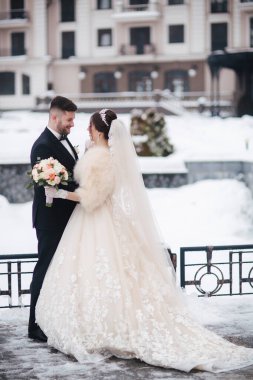 Düğün çifti kışın dışarıda yürüyor. Güzel gelin ve yakışıklı sakallı damat. Her yer karla kaplı.